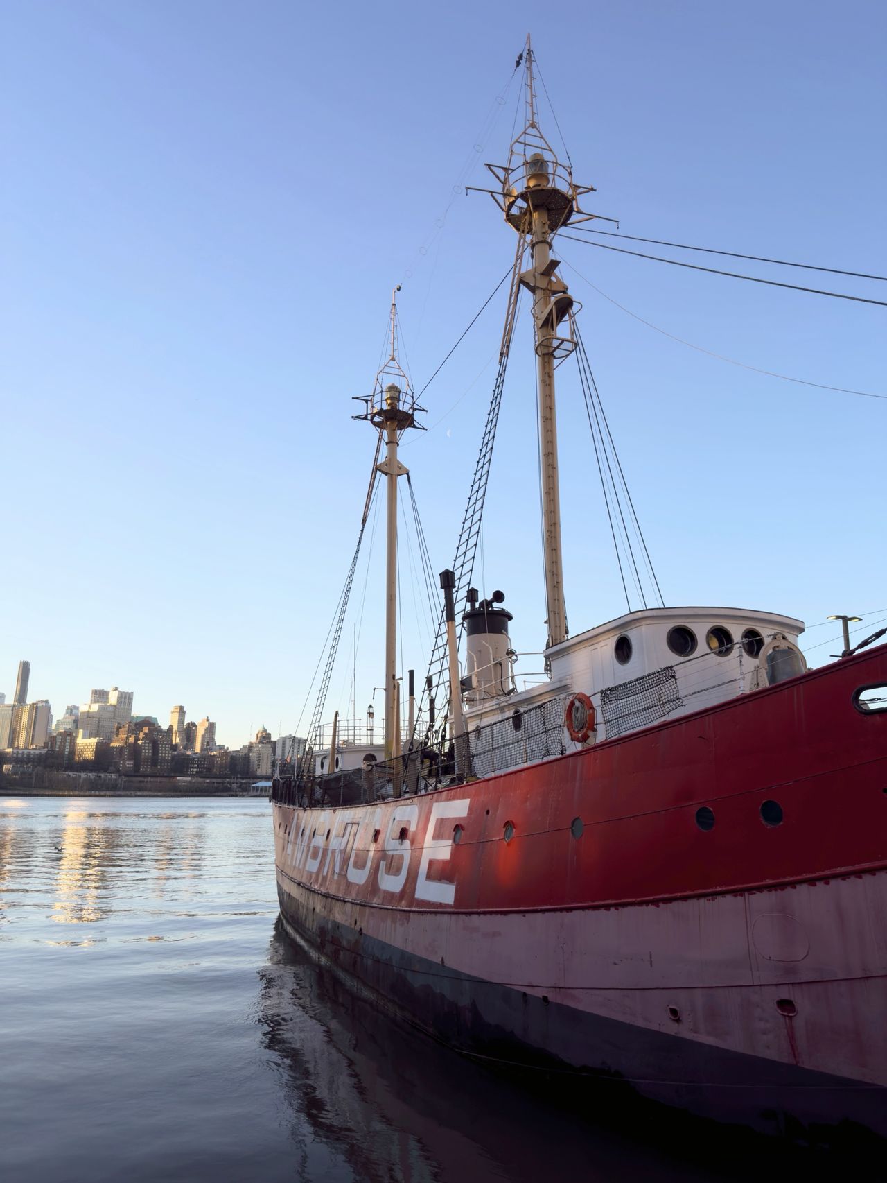 The red Ambrose lightship docked at South Street Seaport with the lower Manhattan skyline behind it.