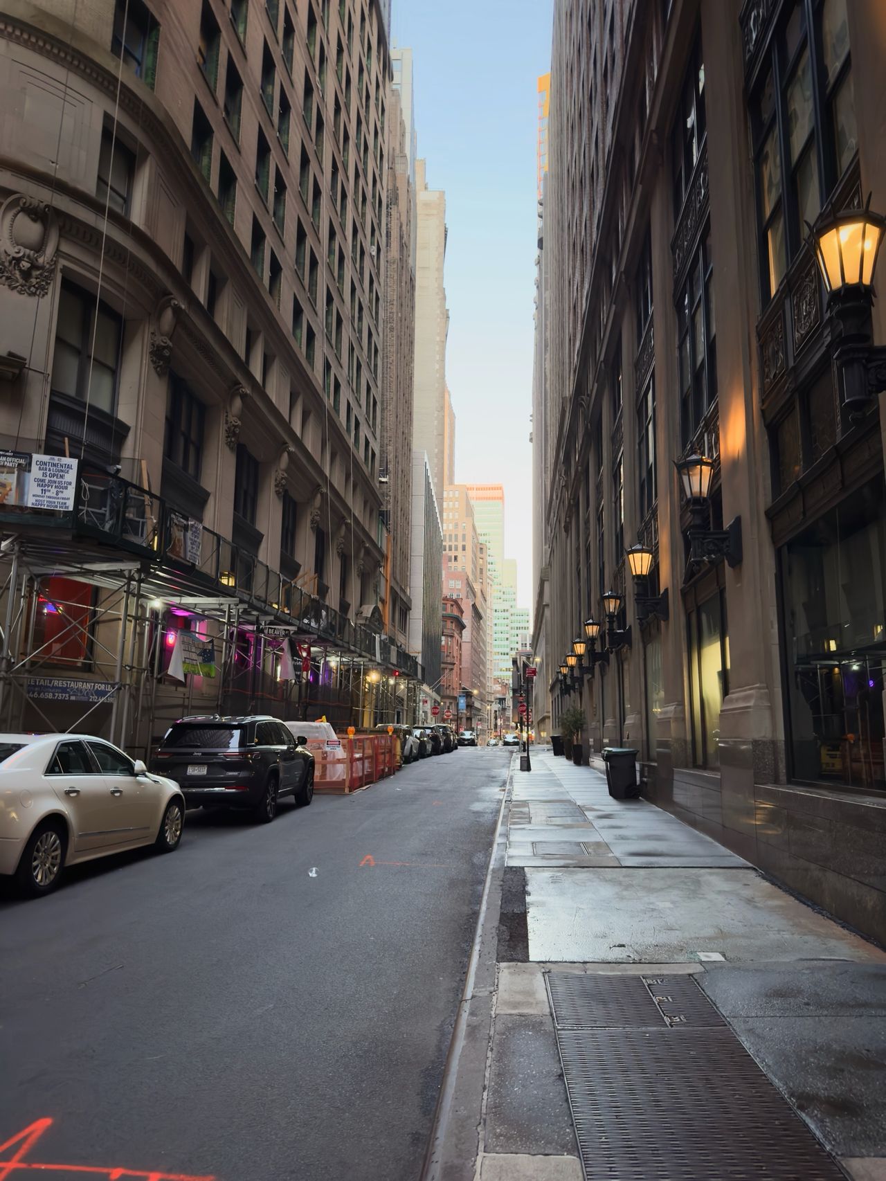 A narrow city street lined with tall buildings and warm wall-mounted lights.