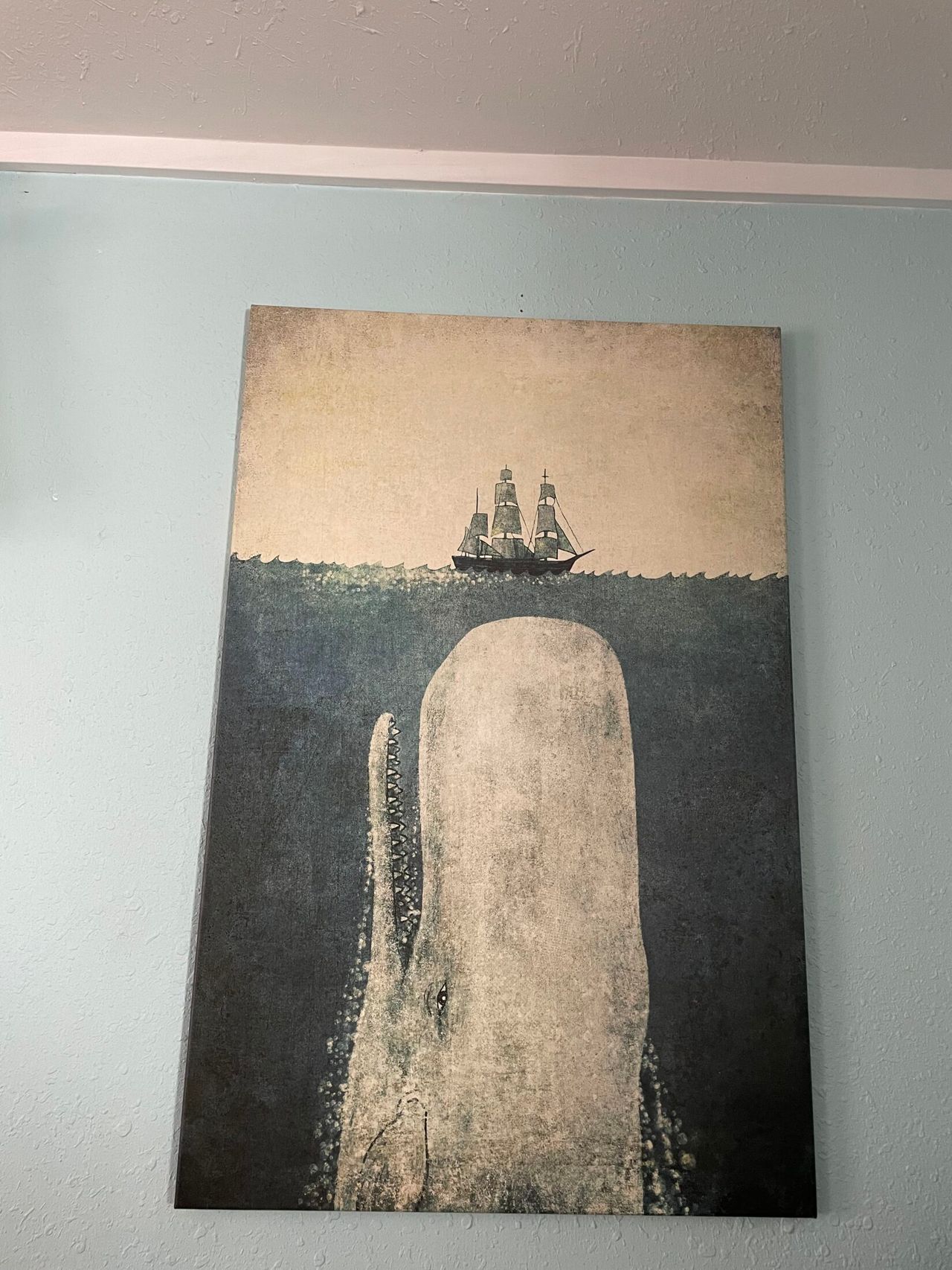 A print of a giant whale below water and a small ship above. It looks like the whale is about to eat the ship.