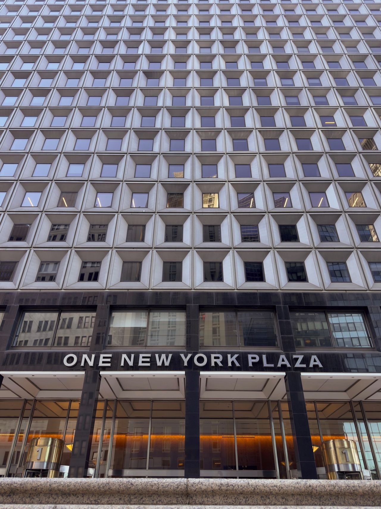 Looking up at One New York Plaza, a tall office tower with a grid of recessed square windows repeating across its facade