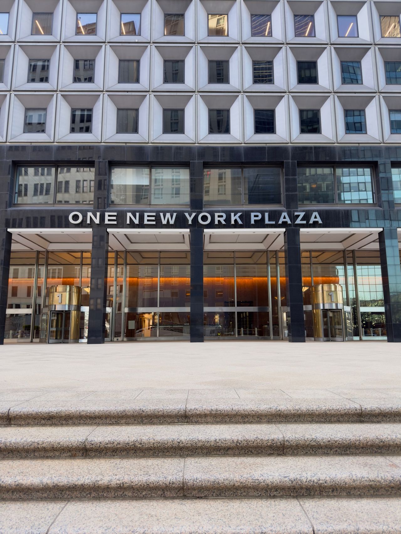 Granite steps and plaza leading up to the entrance of One New York Plaza, with revolving doors and the repeating window grid above