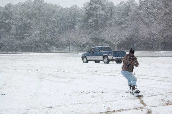 Someone gets pulled on a snowboard behind a blue truck.