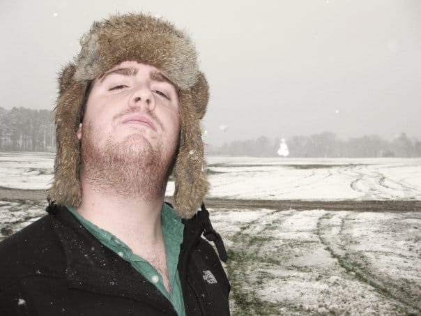 Patrick in a furry hat looking confident with tire marks in the snow.