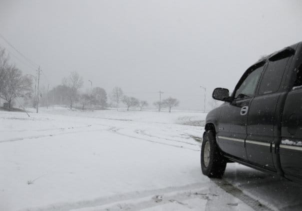 A black truck in the foreground. A snowy hill in the distance.