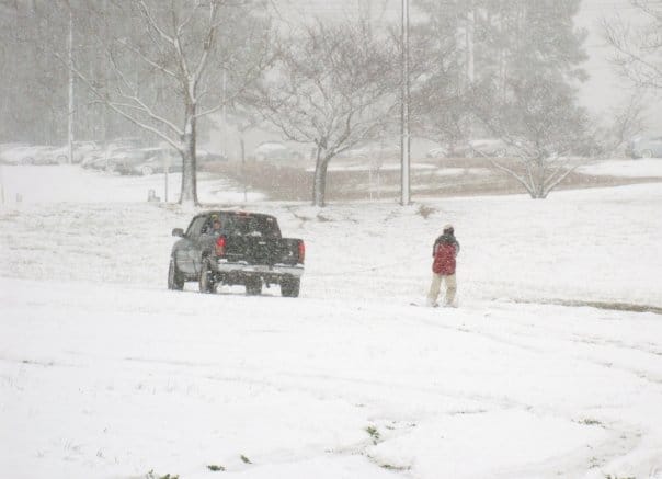 A black truck pulls someone behind it with a snowboard attached.