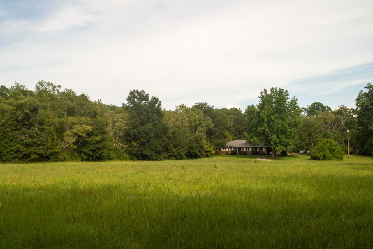 A field in the country with a small brick house in the distance.