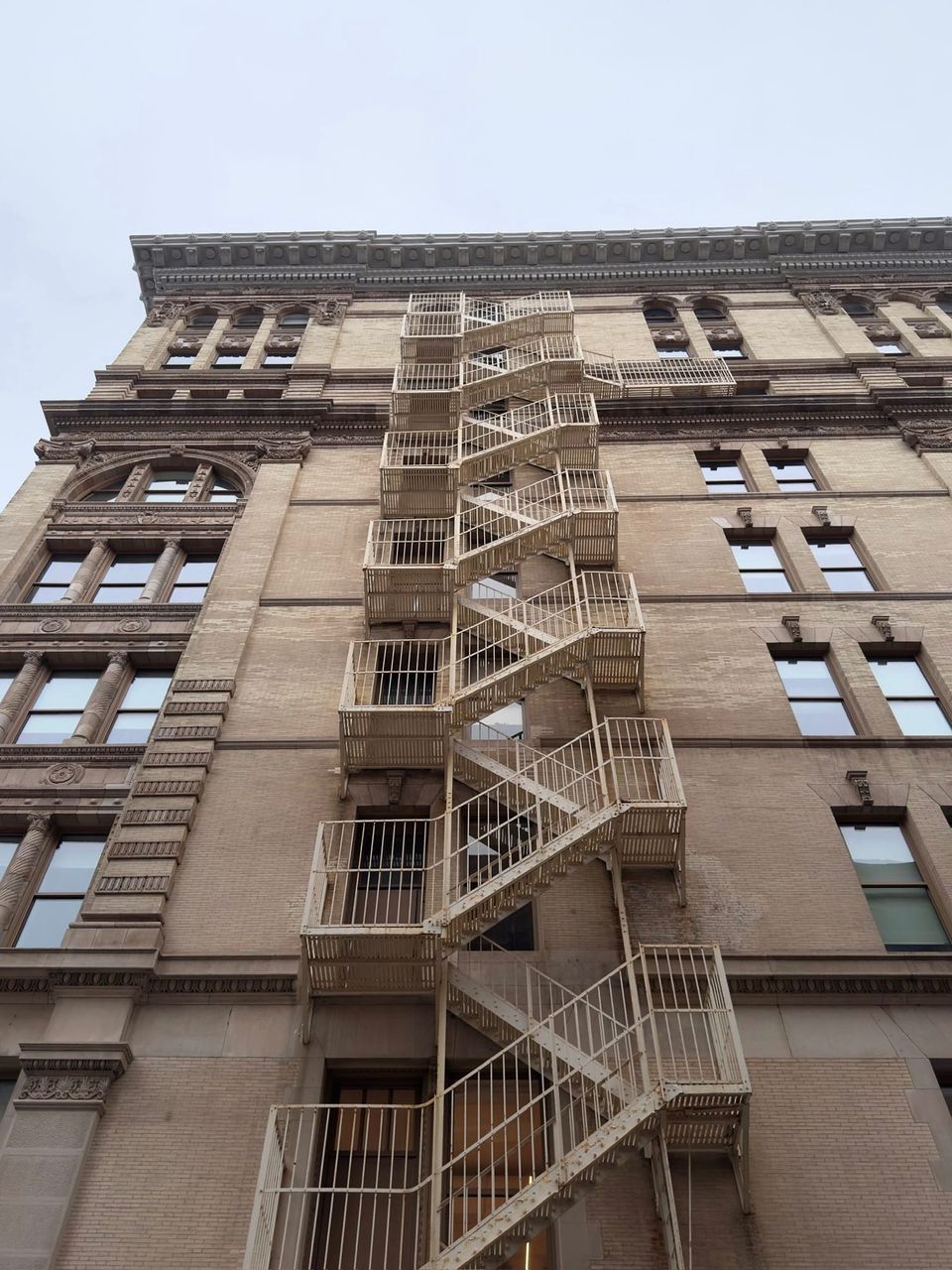 Cream fire escape zigzagging up a tan brick building