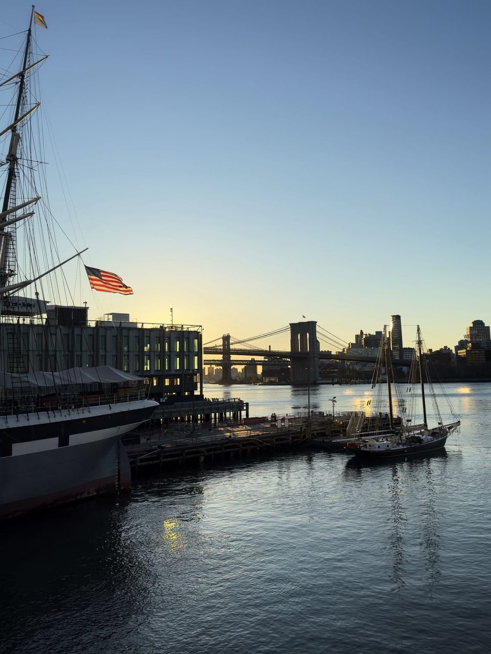Tall ship bow and American flag at South Street Seaport with the Brooklyn Bridge at sunrise