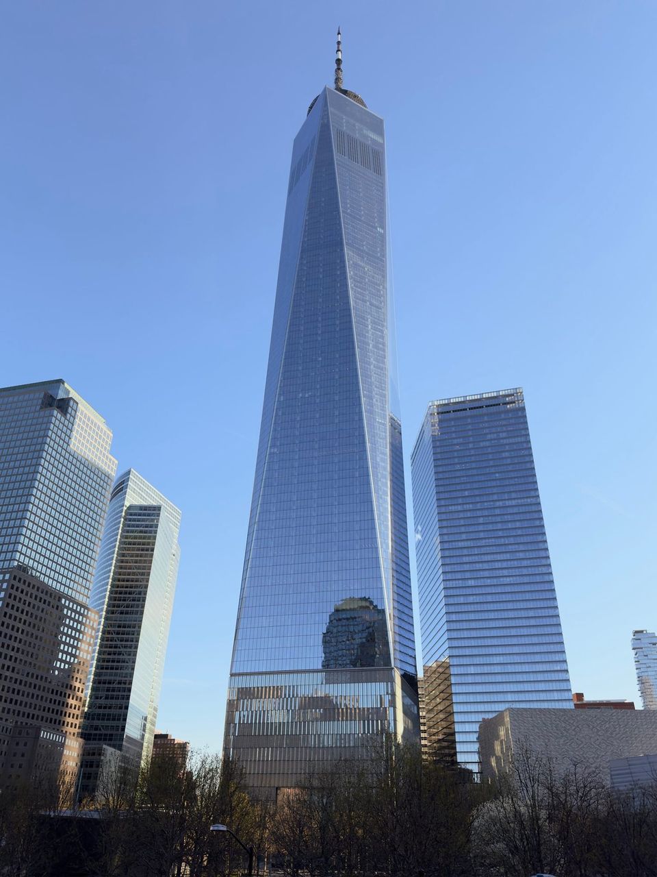 One World Trade Center rising above neighboring glass towers against a blue sky