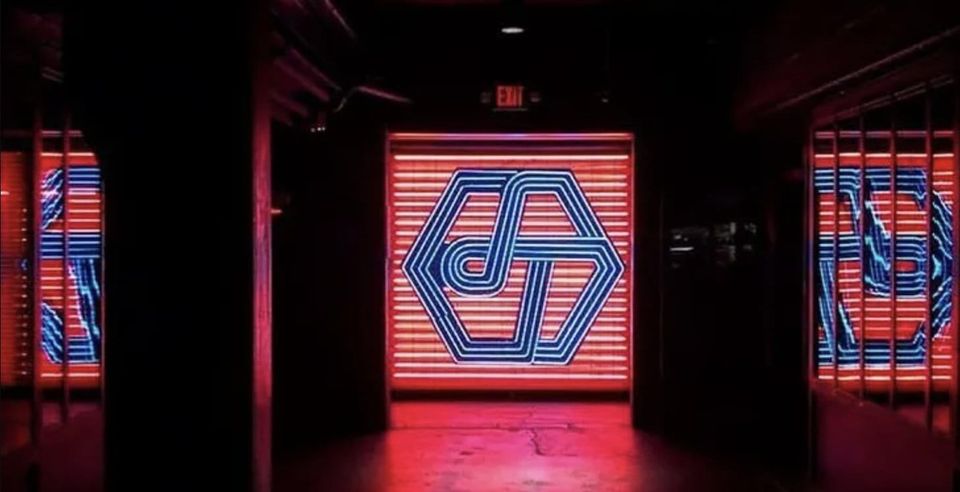 A dark corridor with glowing red panels and a large blue geometric logo