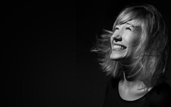 Black-and-white portrait of a laughing woman with windswept blonde hair against a dark background