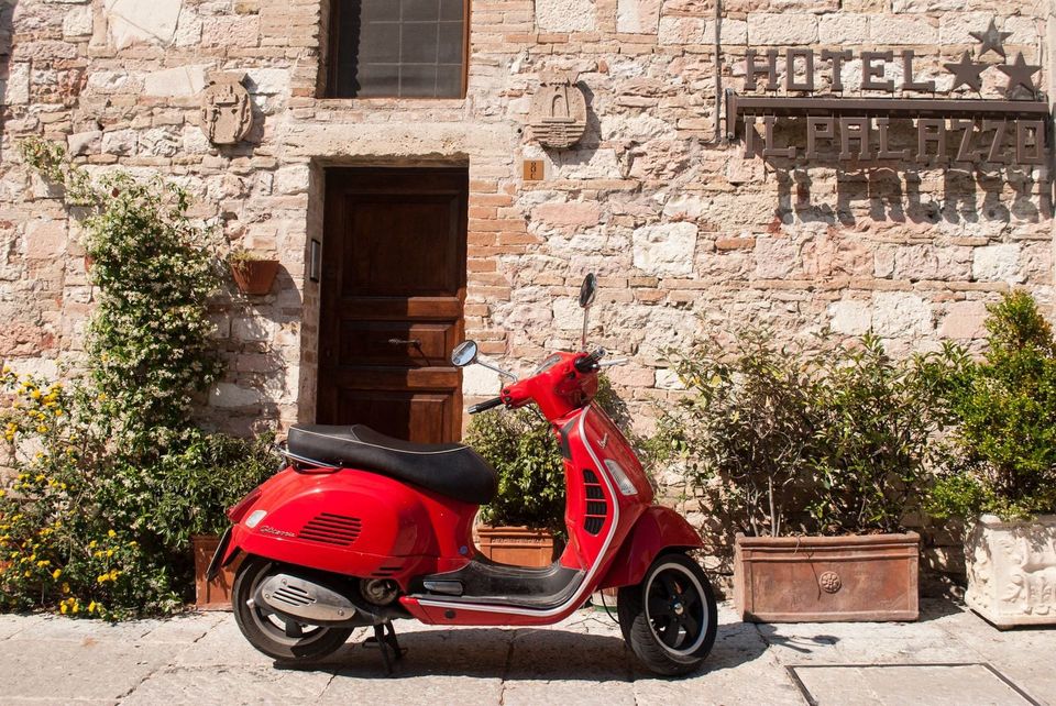 Red Vespa scooter parked in front of a wooden door on the stone wall of Hotel Il Palazzo