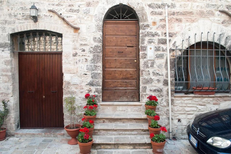 Arched wooden door on a stone Italian building with steps lined by pots of red geraniums